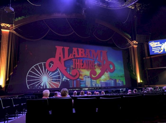 The image shows the interior of a theater with a large screen displaying "Alabama Theatre" and an illustration of a Ferris wheel and skyline.