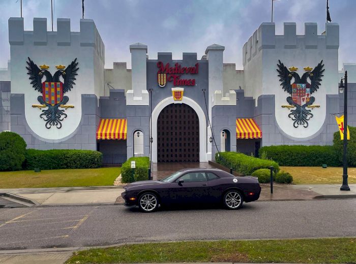 A building resembling a medieval castle, with two large crests on its exterior walls, flags flying, and a black car parked in front of it.