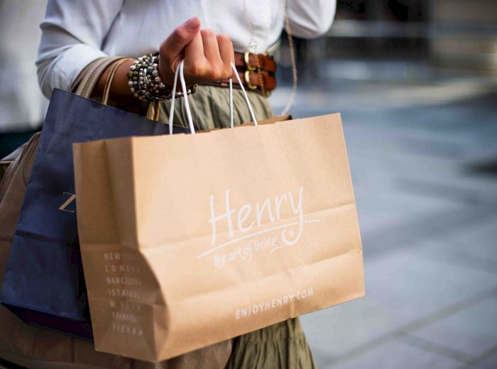 A person is holding a brown shopping bag with the word "Henry" on it, along with additional shopping bags, displaying bracelets on their wrist.