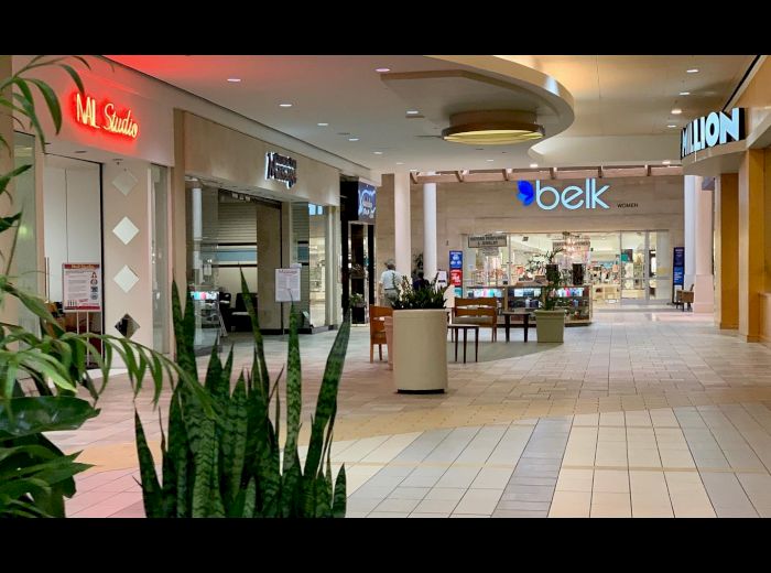 The image shows the inside of a mall with stores, including Belk and LION, with a few plants and seating areas in the center.