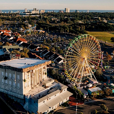 The image shows an amusement park with a Ferris wheel, an upside-down building, colorful buildings, and a distant city skyline against a clear sky.